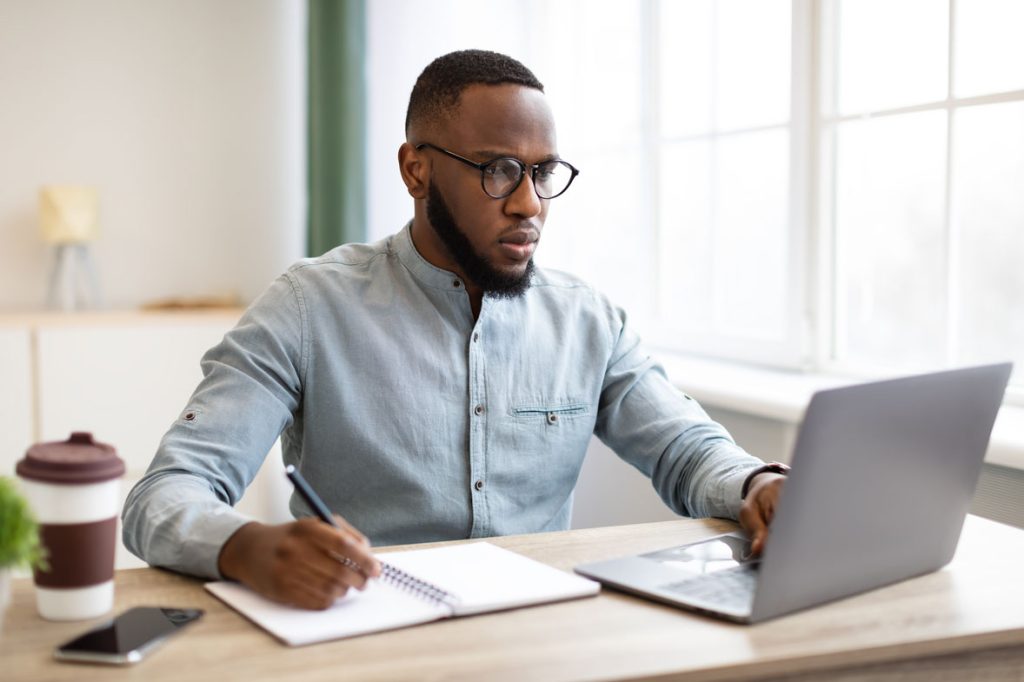 african-business-guy-working-on-laptop-taking-note